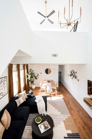 A modern living room with a black sofa, a round coffee table, and a dining area with a wooden table and chairs.