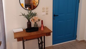 Una habitación con puerta azul, una mesa de madera con espejo, un florero con flores y un dispositivo blanco sobre la mesa.