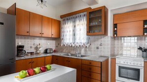 Una cocina moderna con armarios de madera, encimera blanca, horno integrado y una ventana con cortina estampada.