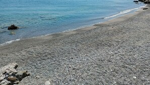 Una playa de guijarros con agua azul cristalina y colinas a lo lejos.