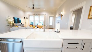 A modern kitchen with white cabinetry, a stainless steel dishwasher, and a large island with a sink. - Gulf Views, 4BR/4BA w/ Game Room, Private Pool w/ Heat, EV Charger (St. George Island)