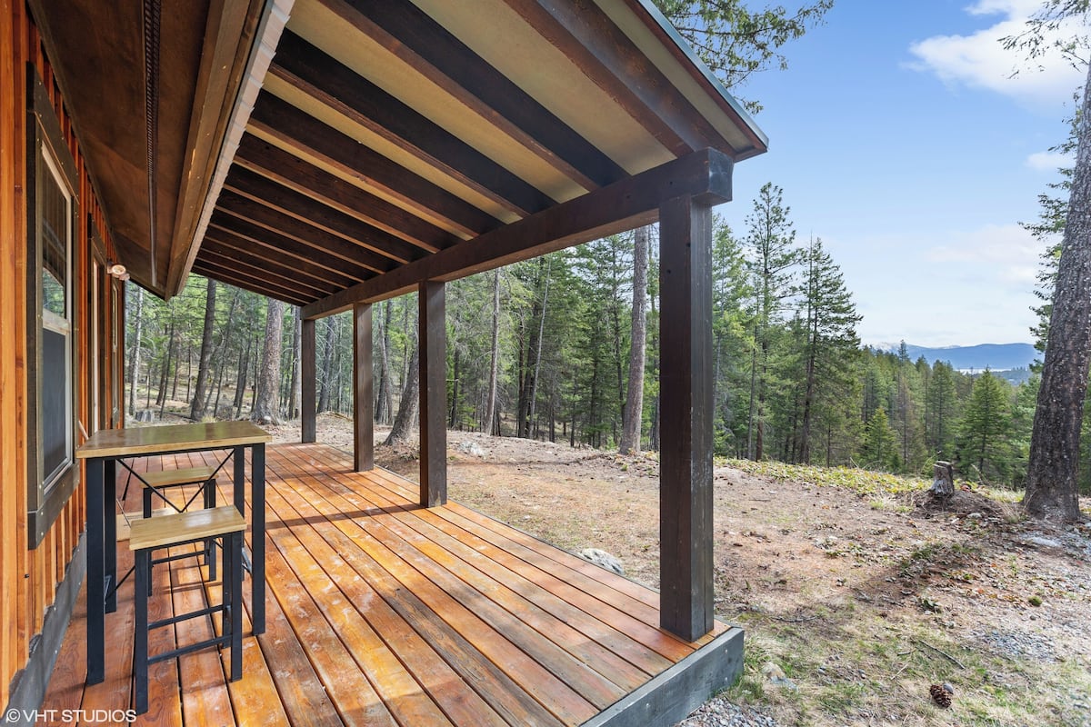 A wooden deck with a table and benches, surrounded by a forested area.