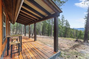 A wooden deck with a table and benches, surrounded by a forested area.