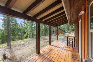 A wooden deck with a table and chairs, surrounded by forested area.