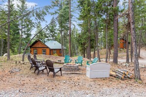 A cabin with a fire pit and outdoor seating, surrounded by a forest.