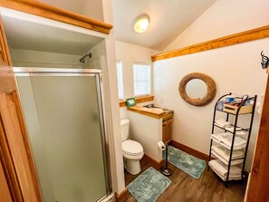 A bathroom with a shower, toilet, sink, and a towel rack.