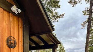 A wooden cabin with a 'Welcome' sign, a gravel driveway, and a forested backdrop.