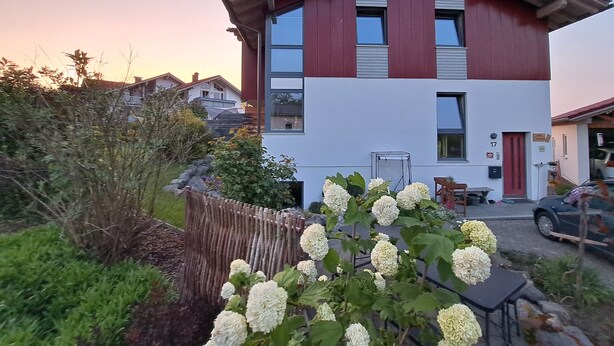 Ein modernes, zweistöckiges Haus mit rotem und weißem Anstrich, der Hausnummer '17' und einem Garten mit Hortensienblüten.