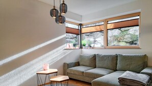 Ein modernes Wohnzimmer mit einer Eckcouch, einem kleinen Holztisch und einem runden Teppich. Drei Pendelleuchten hängen über dem Tisch.
