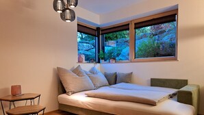 Ein modernes Schlafzimmer mit Bett, einem kleinen Tisch und einem Fenster mit Blick auf Felsen und Grün.