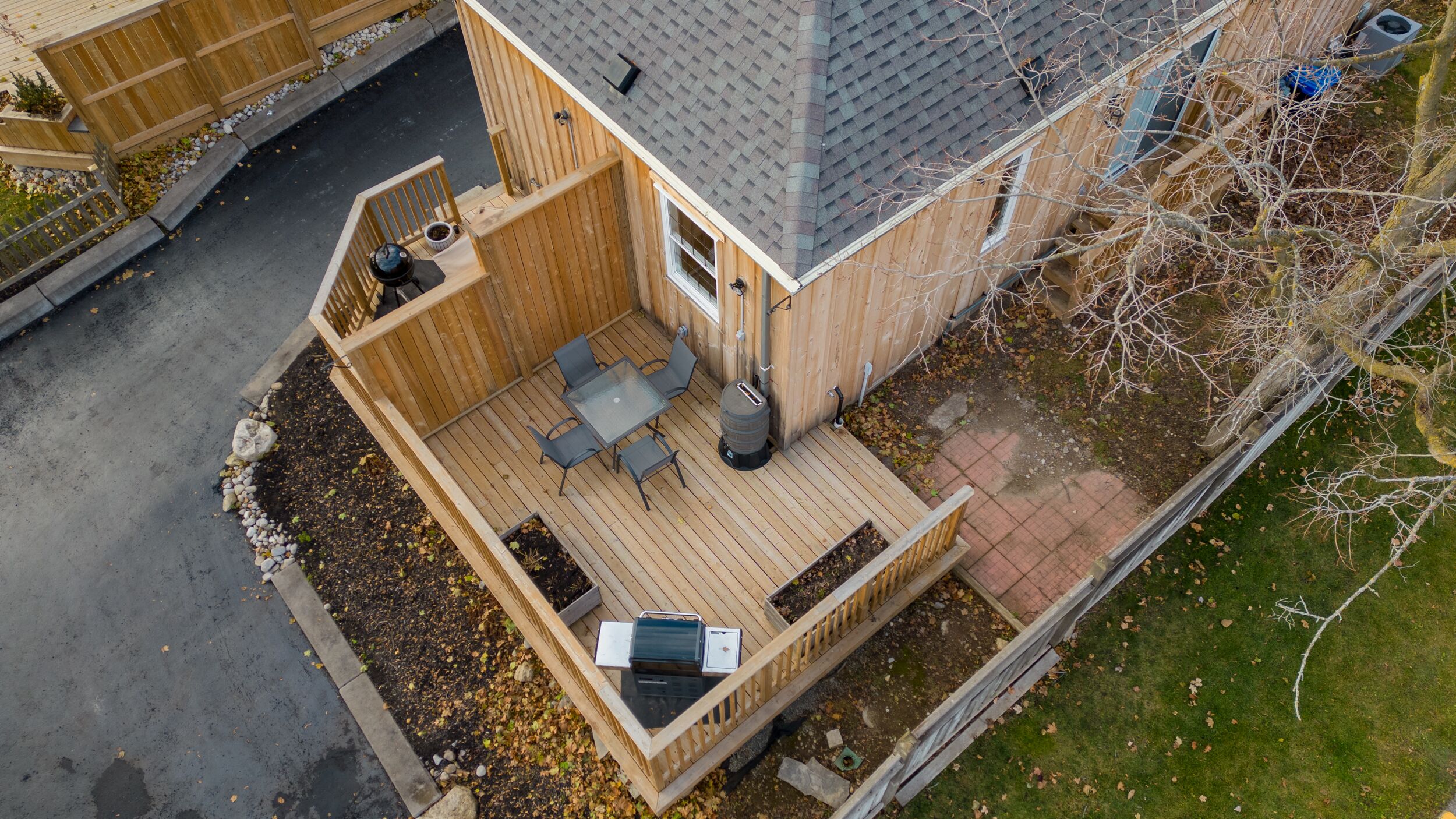 Vue aérienne d’une terrasse en bois avec une table et des chaises, entourée d’un jardin agrémenté d’un petit étang et d’une clôture en bois.