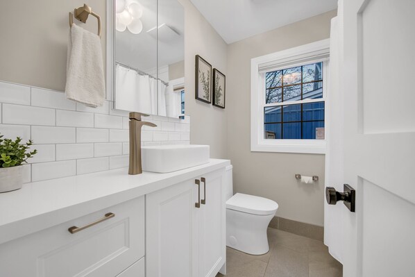 Une salle de bain moderne avec des meubles blancs, un lavabo blanc, un miroir, des toilettes et une fenêtre donnant sur l’extérieur.