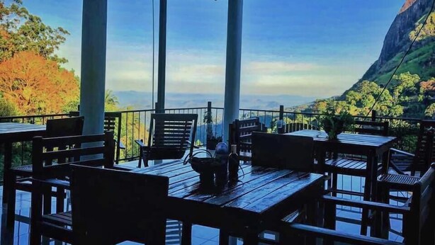 A covered outdoor seating area with tables and chairs, overlooking a mountainous landscape. - Dewy Arena Hotel (Ella)