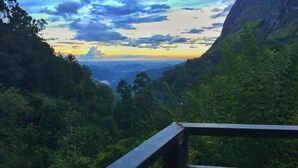 A view from a wooden deck overlooking a lush valley with dense vegetation and distant mountains under a partly cloudy sky. - Dewy Arena Hotel (Ella)