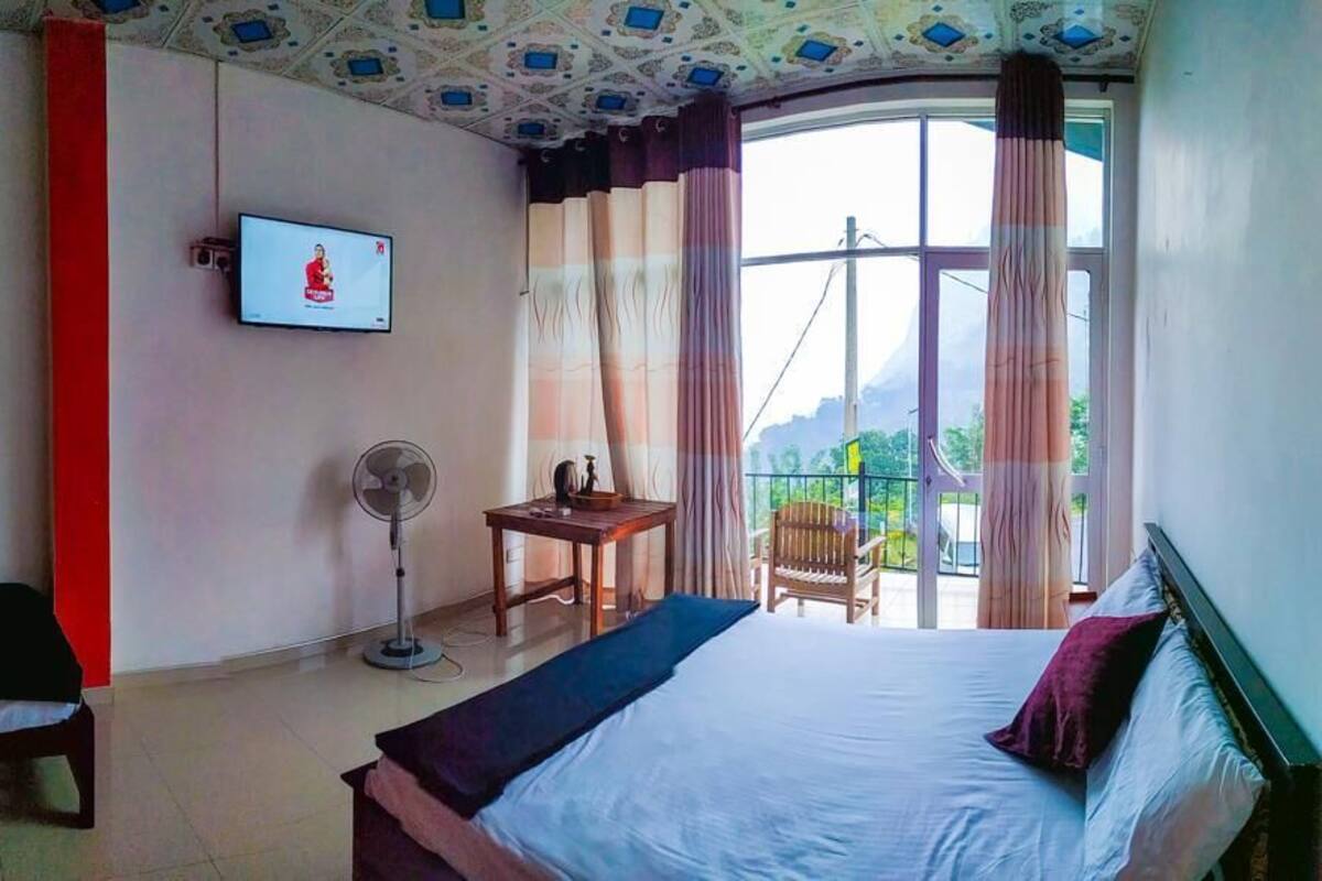 Habitación de hotel con cama, escritorio, silla, televisión y balcón con vistas.