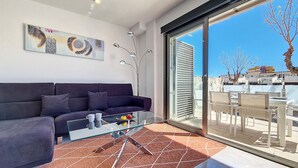 Uma sala de estar moderna com um sofá escuro, uma mesa de centro de vidro e uma grande porta de correr de vidro que dá para um espaço ao ar livre.