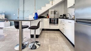 Uma cozinha moderna com uma ilha central, eletrodomésticos de aço inoxidável e uma escada que leva a um andar superior.