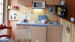Cozinha compacta com armários de madeira, micro-ondas, cafeteira e mesa de madeira.
