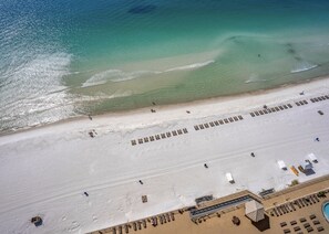 An aerial view of a beach with rows of sun loungers and a pool area.