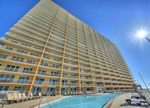 A high-rise hotel with multiple balconies, a swimming pool, and sun loungers.