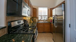 A kitchen with wooden cabinets, a stainless steel refrigerator, a stove, and a window with blinds. - Donner Lake, Home | Walk to the Lake, Trails, & Family Activities (Truckee)