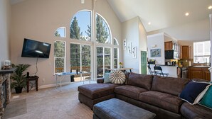A spacious living room with a large sectional sofa, a flat-screen TV mounted on the wall, and a dining area with a table and chairs. - Donner Lake, Home | Walk to the Lake, Trails, & Family Activities (Truckee)