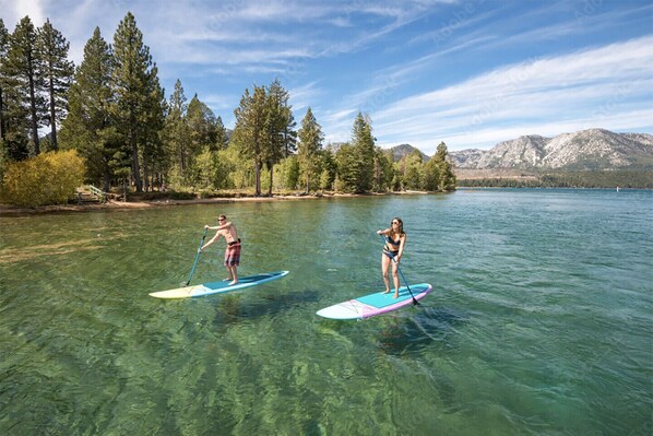 Deux personnes pratiquent le paddle sur un lac aux eaux claires, avec des montagnes en arrière-plan.
