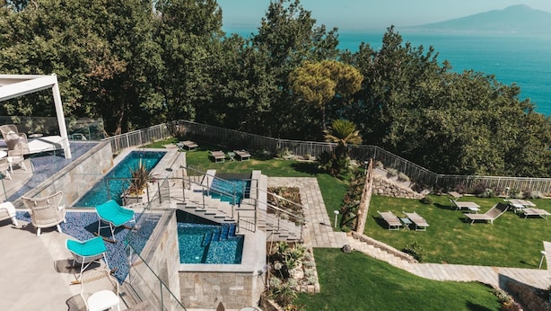 Ein Poolbereich auf dem Dach mit mehreren Pools, Liegestühlen und Meerblick.
