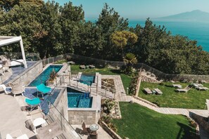 A rooftop pool area with multiple pools, lounge chairs, and a view of the sea.