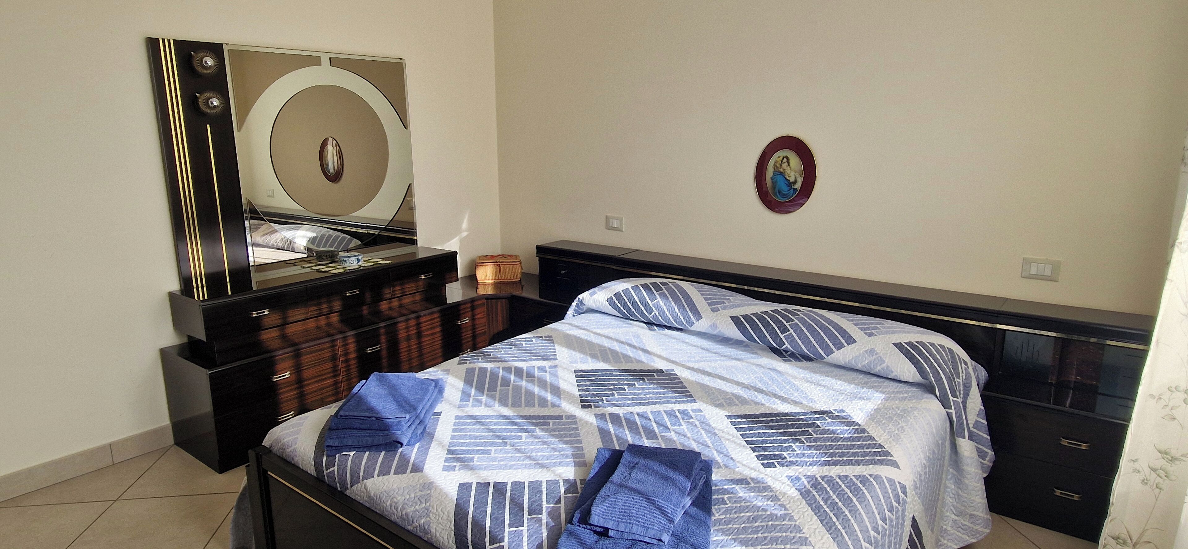A bedroom with a bed, a dresser, a mirror, and a wall decoration.