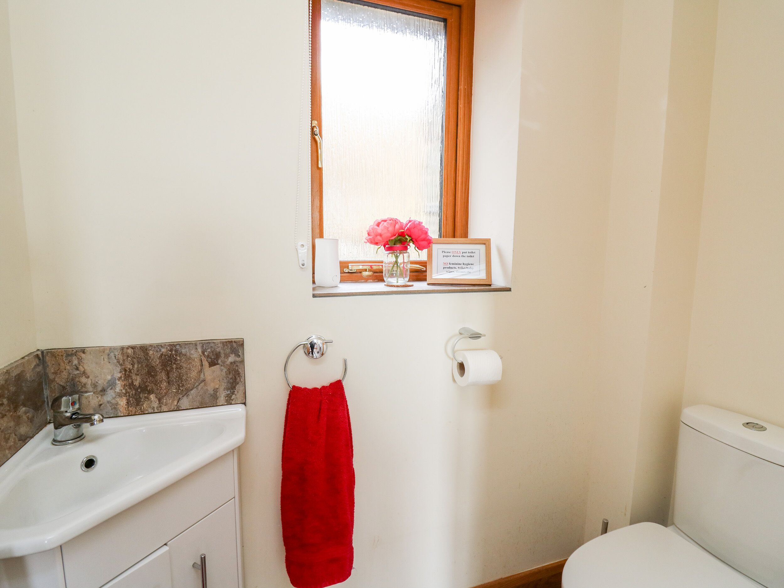 A bathroom with a sink, toilet, and a window with a vase of flowers.