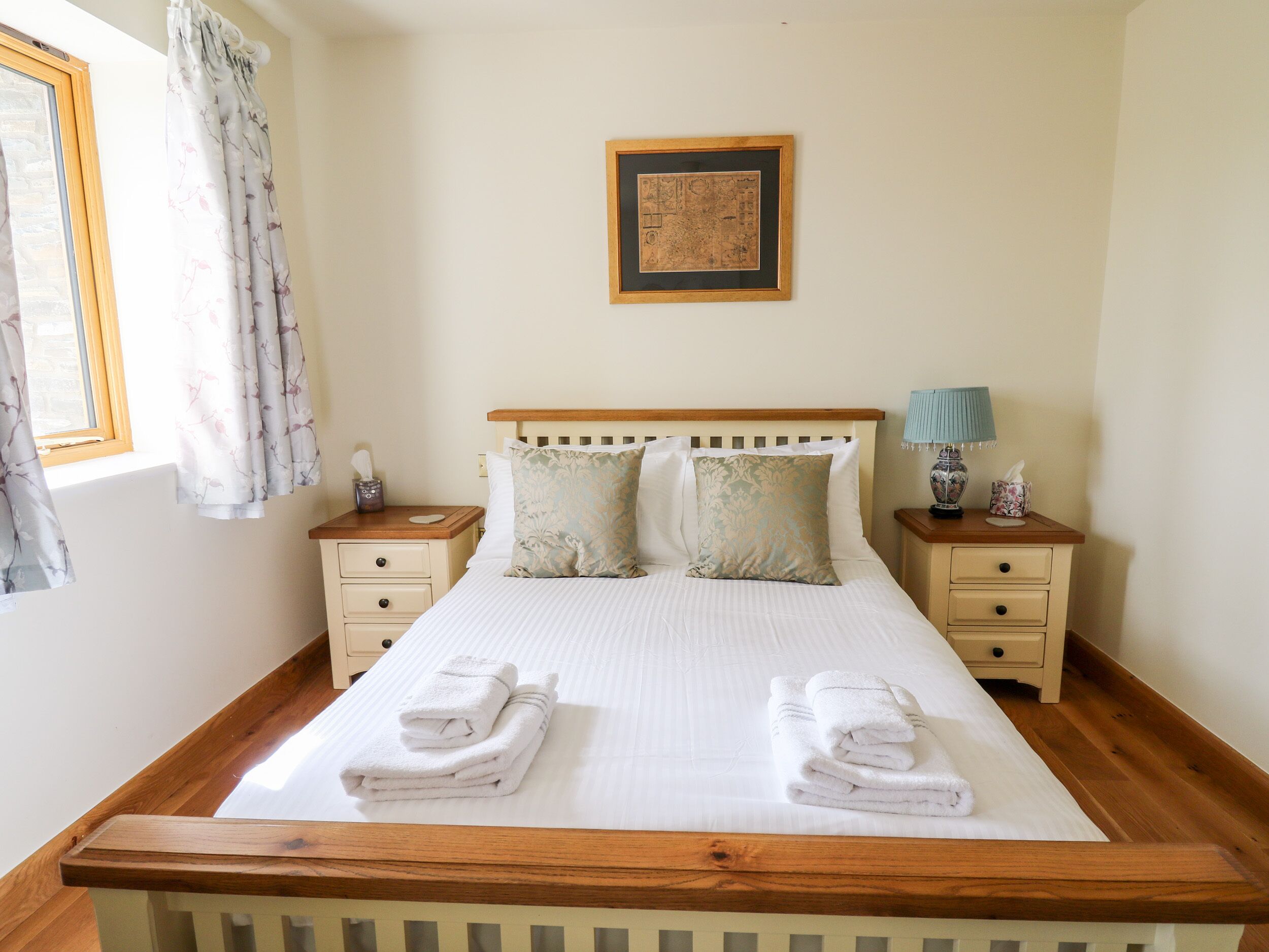 A neatly made bed with two pillows, a wooden headboard, and two nightstands with lamps and small decorative items.