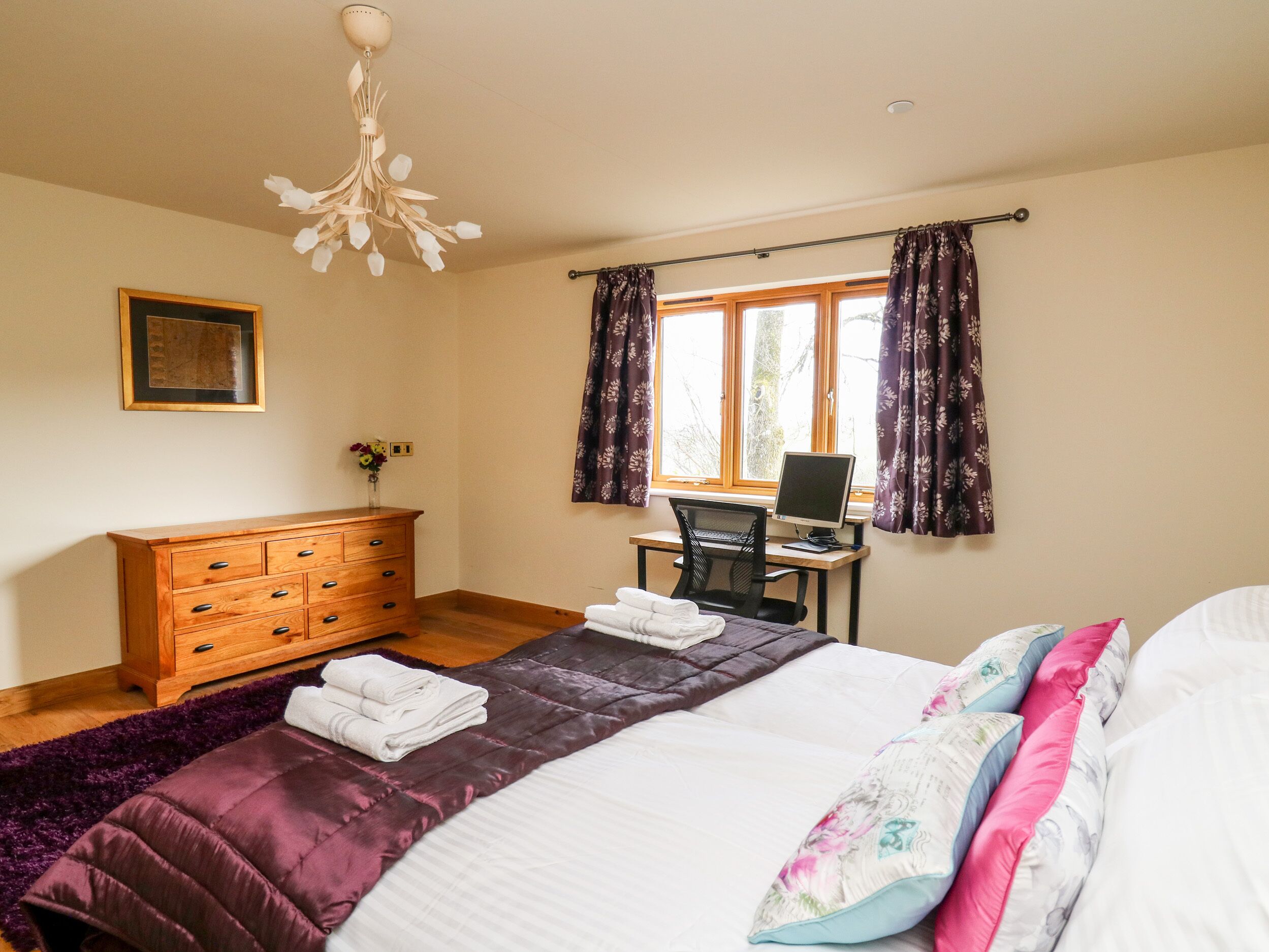 A bedroom with a bed, a desk with a computer, a dresser, and a window with curtains.