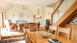 A spacious living room with a wooden dining table, chairs, a glass bowl, and a staircase. - The Orchard (Knighton)