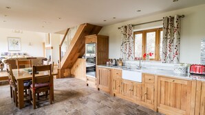A spacious kitchen with wooden cabinets, a built-in oven, and a large window with floral curtains. - The Orchard (Knighton)