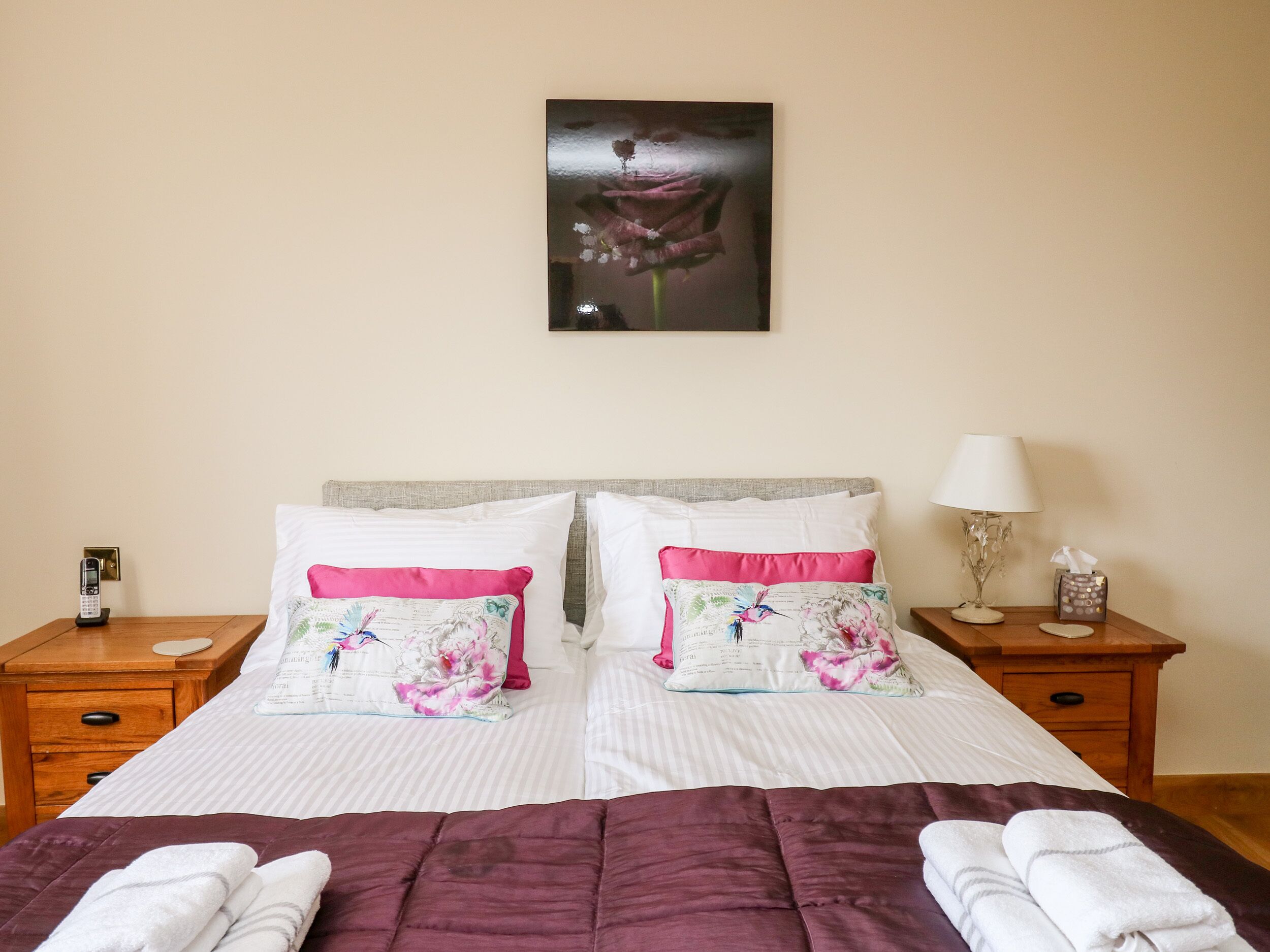 Un lit bien fait, recouvert d’une couvre-lit violette, avec deux oreillers ornés de motifs floraux, une lampe de chevet et une petite table sur laquelle se trouvent un téléphone et une boîte de mouchoirs.