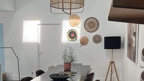 Ett modernt kök med ett träbord, stolar, en hängande lampa och diverse köksredskap.