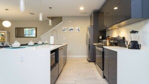 Une cuisine moderne dotée d’un îlot central, d’appareils électroménagers en acier inoxydable et de luminaires suspendus.