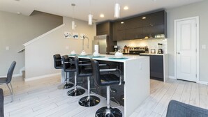 Une cuisine moderne dotée d’un îlot central, de tabourets de bar et de luminaires suspendus.