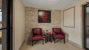 A reception area with a stone wall, two red chairs, a small table with decorative items, and a sign reading 'Red Roof Inns & Suites'. - Red Roof Inn & Suites Vineland - Buena (Buena)