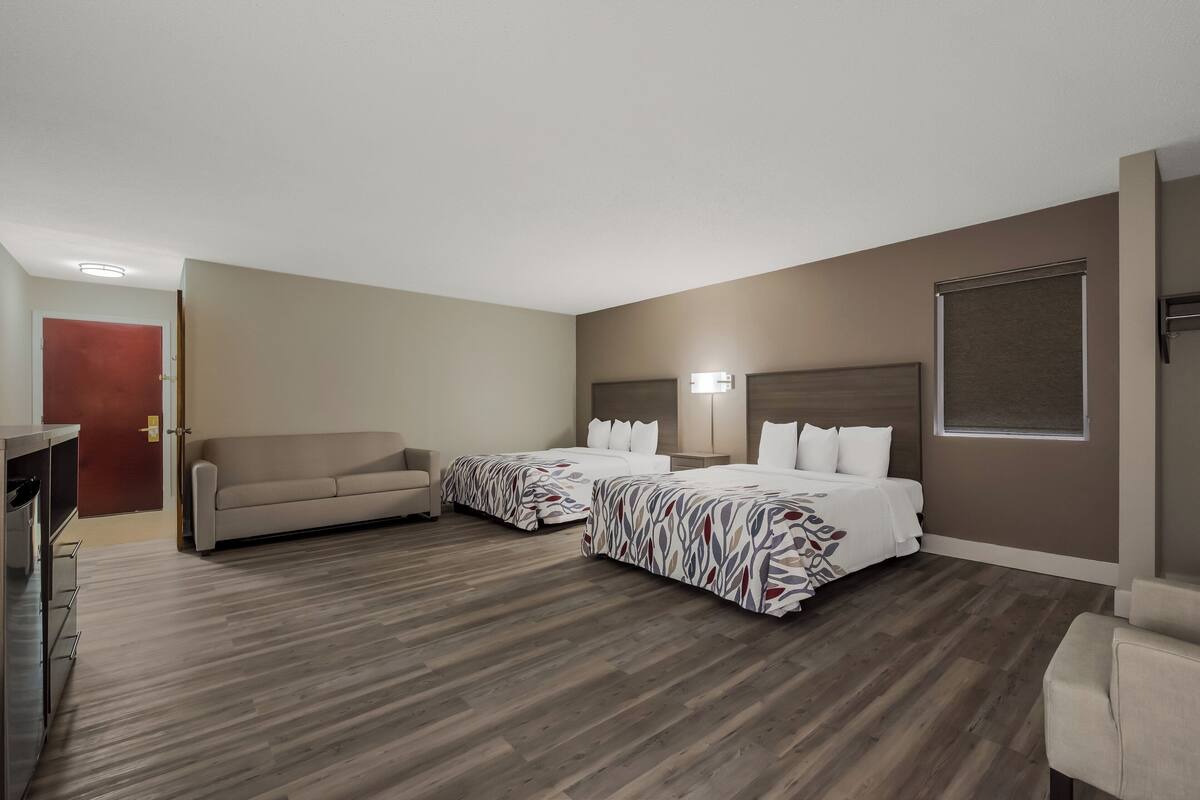 A hotel room with two beds, a sofa, a desk, and a window.