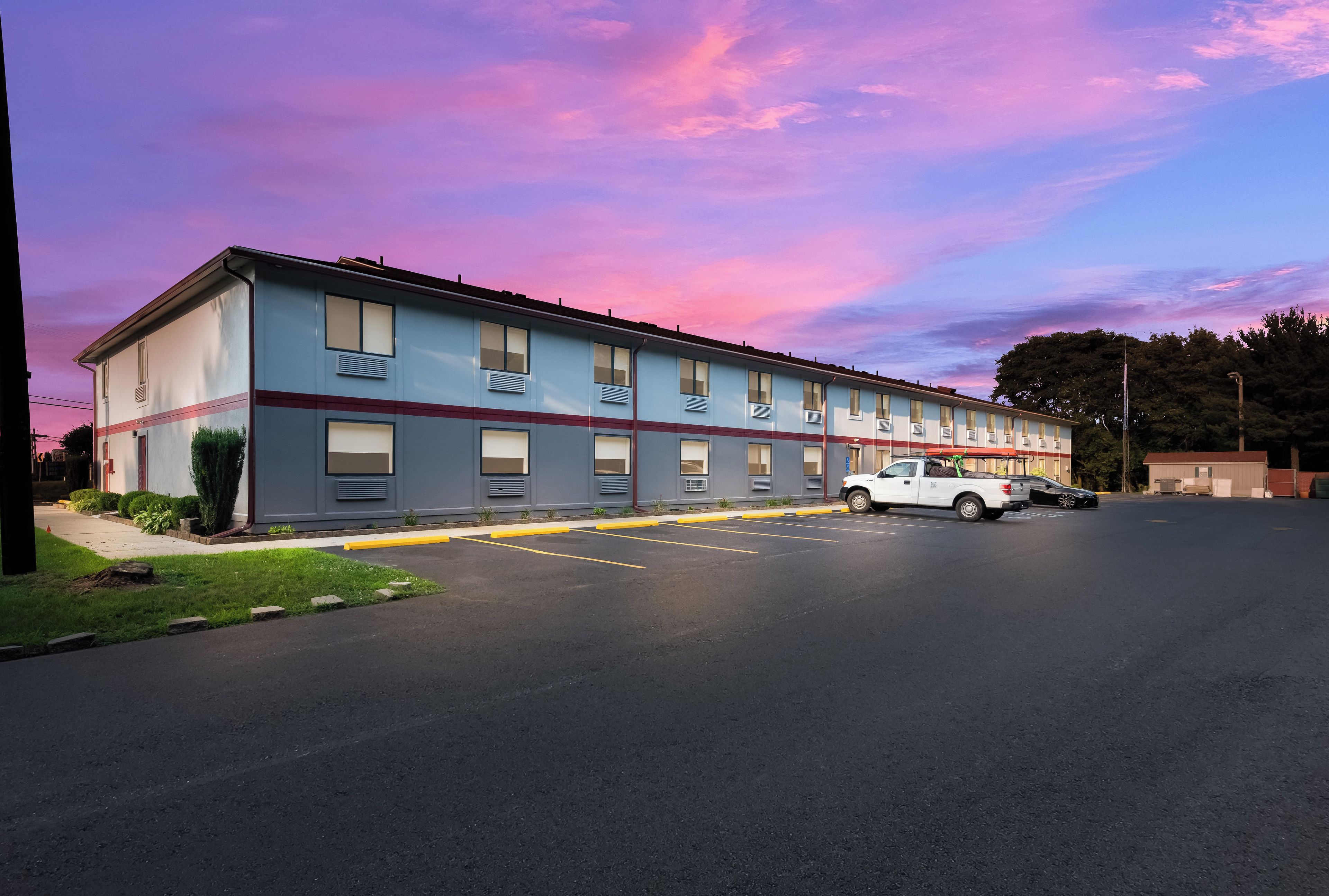A two-story motel with a row of rooms, a parking lot, and a clear sky.