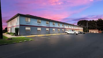 A two-story motel with a row of rooms, a parking lot, and a clear sky.