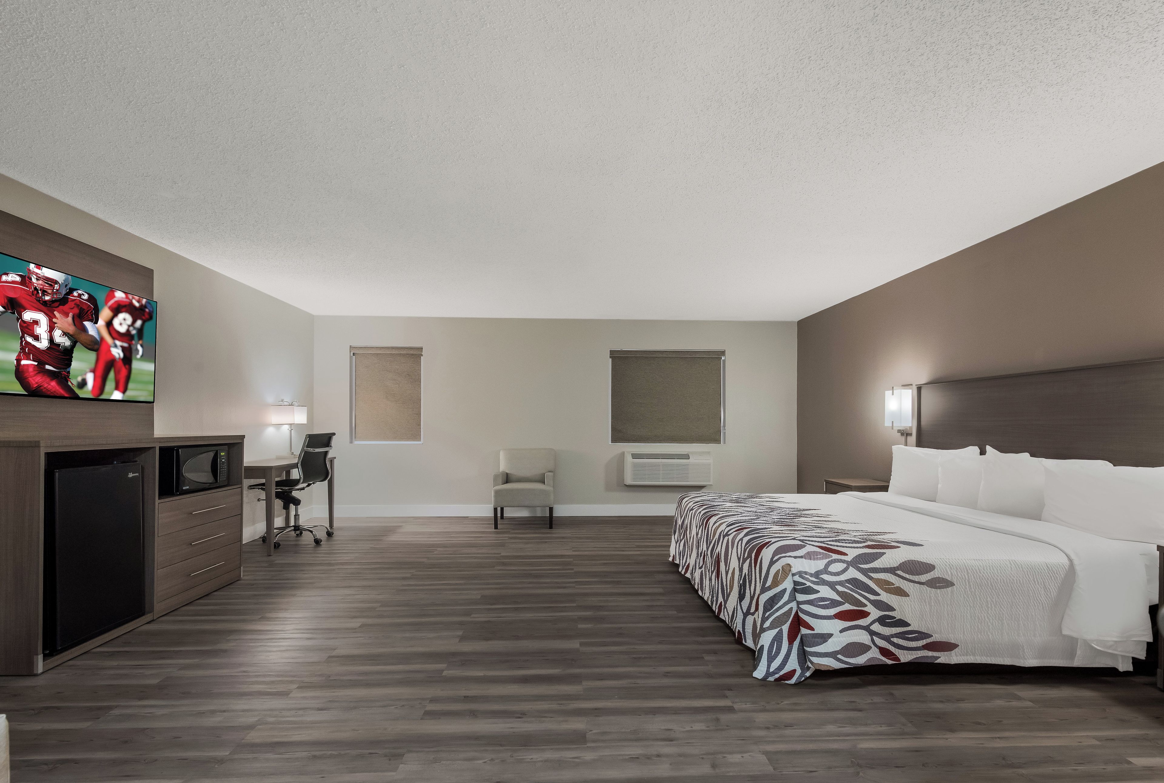 A hotel room with a bed, a desk, a chair, a television, and an air conditioning unit.