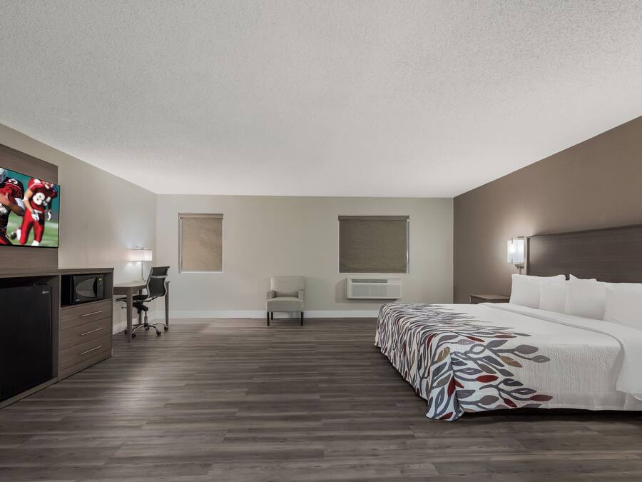 A hotel room with a bed, a desk, a chair, a television, and an air conditioning unit.