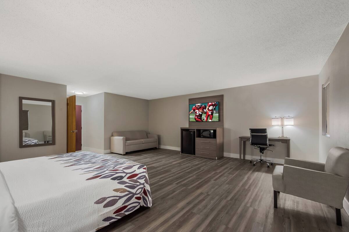 A hotel room with a bed, a desk, a chair, a sofa, and a TV.