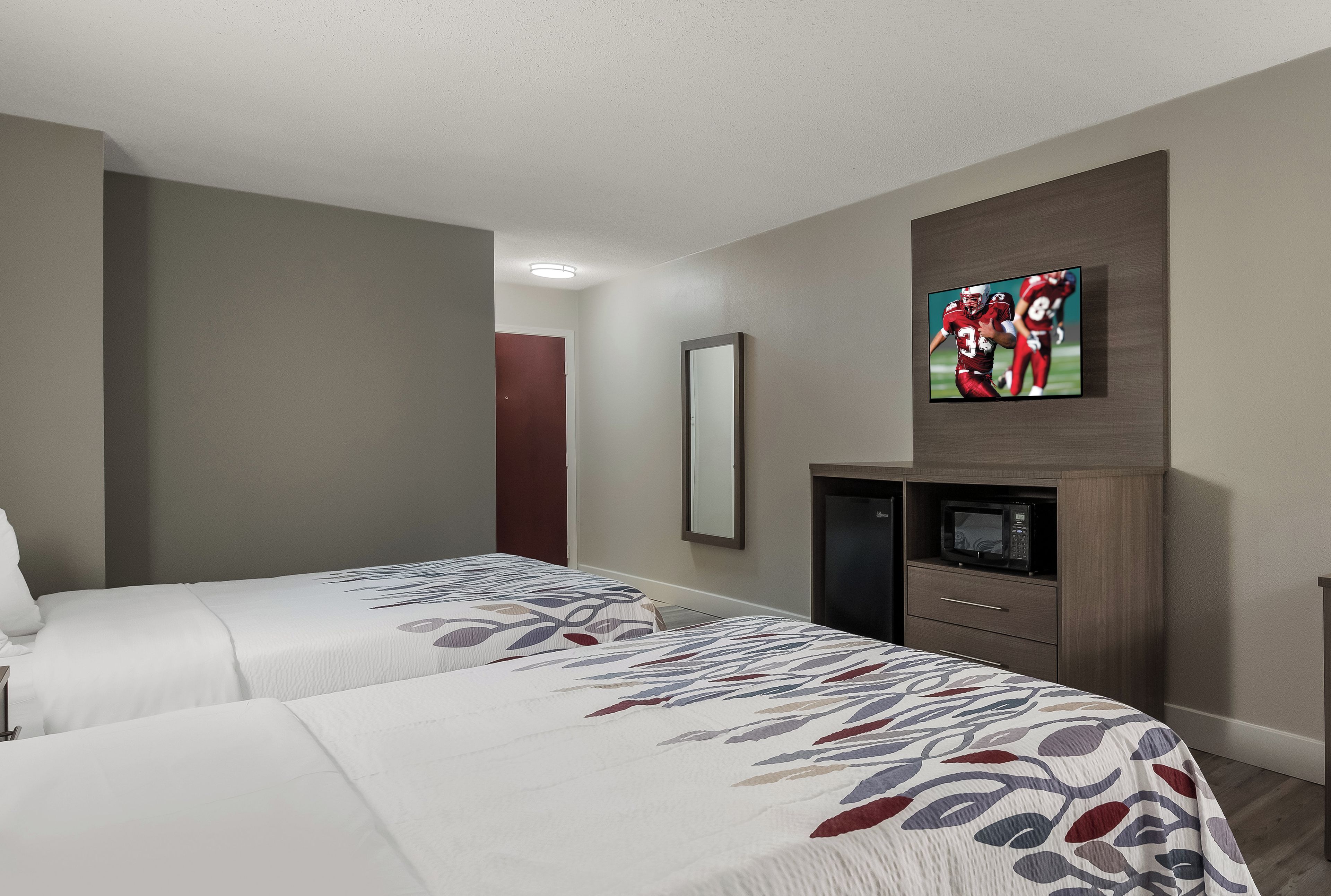 A hotel room with two beds, a TV mounted on the wall, a microwave, and a small cabinet.
