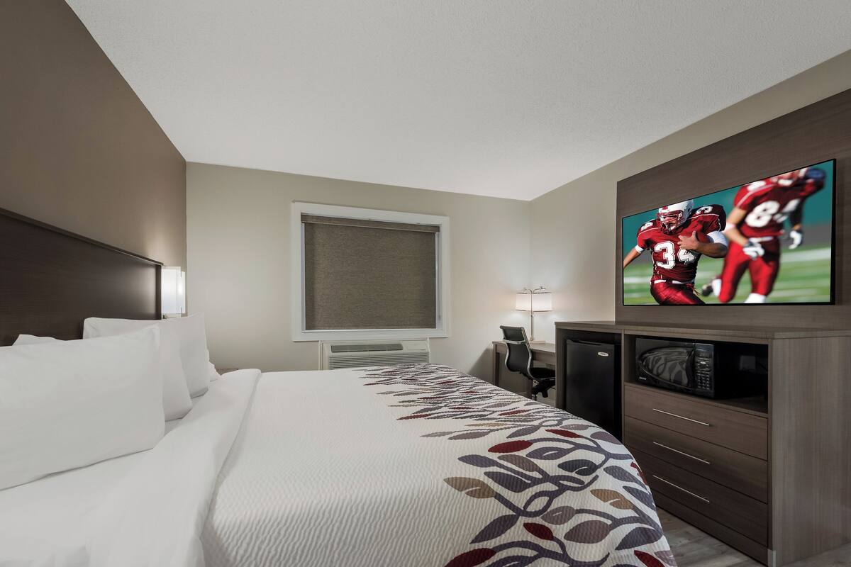 A hotel room with a large bed, a television mounted on the wall, a desk with a chair, and a microwave in the corner.
