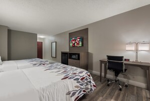 Una habitación de hotel con dos camas, un escritorio con silla, televisión y un reloj.