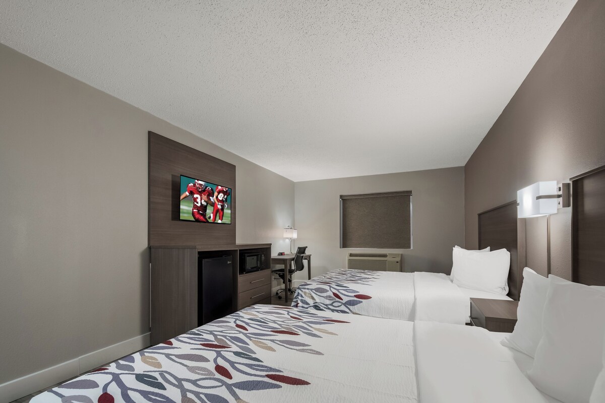 Une chambre d’hôtel avec deux lits, un bureau avec une chaise, un téléviseur fixé au mur et une fenêtre.
